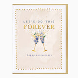 Let's Do This Forever anniversary card with two champagne glasses filled with blue flowers, gold dots, and a brown envelope.